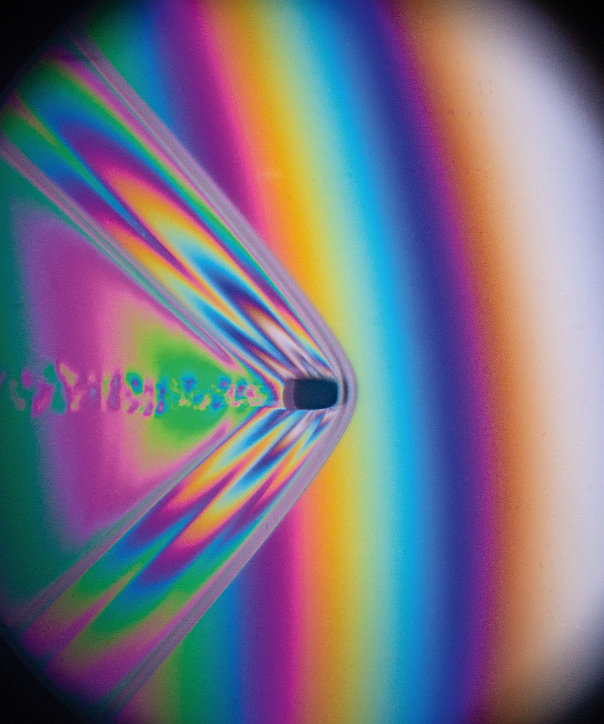 A .22 caliber bullet fired from a rifle flies through the air. This image uses polarizing interferometry to show difference in air pressure, represented by different colors of light. The clear bow wave in front of the bullet shows that it is moving faster than the speed of sound. The exact velocity of this supersonic bullet can be calculated from measurements of the bow wake angle. This image freezes the motion by using a high speed flash with a duration of 1/2,000,000th of a second.