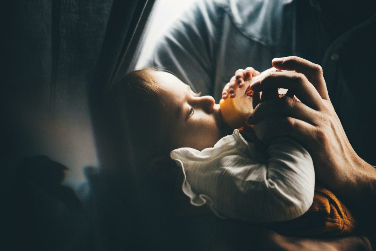 Photo of a parent feeding their baby in their arms with a bottle of milk