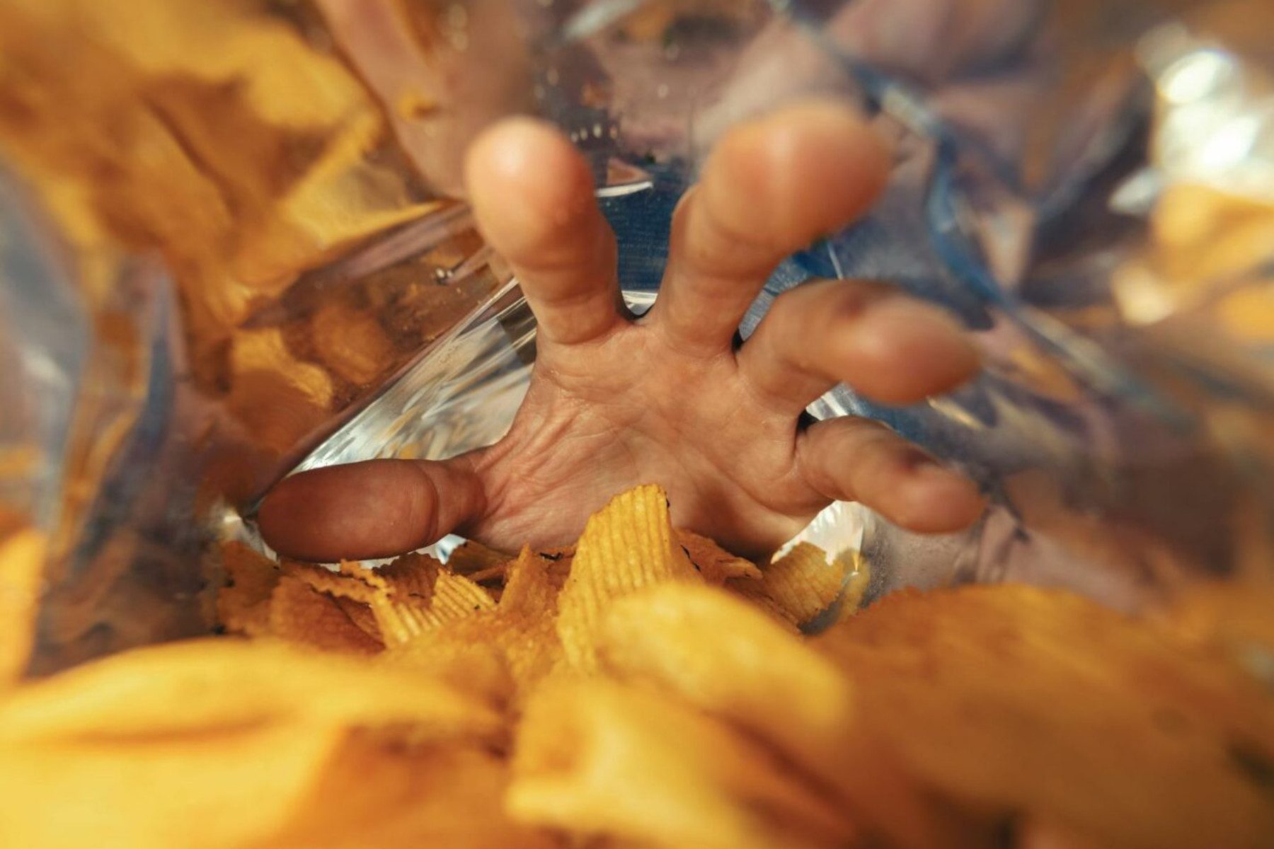 Photo from inside a packet of crisps, a hand reaching in to grab the potatoey crunchy goodness